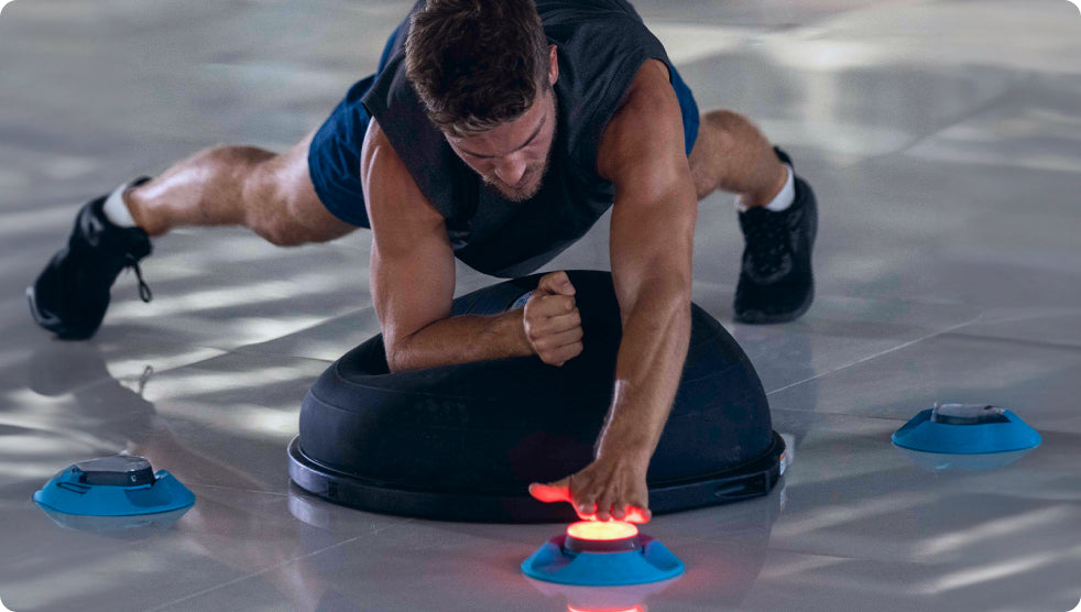 A man using a Bosu ball to enhance his BlazePod workout while tapping out a Pod light