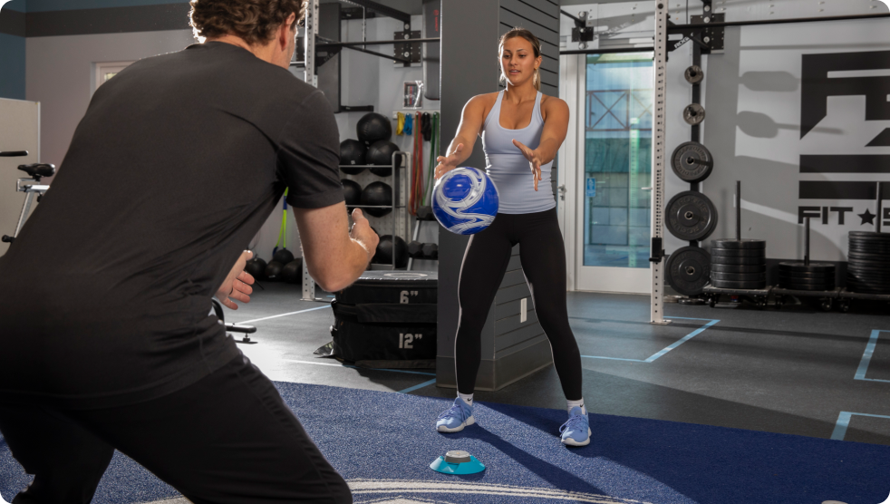 A woman training with a physical therapist with a ball and BlazePod Pods